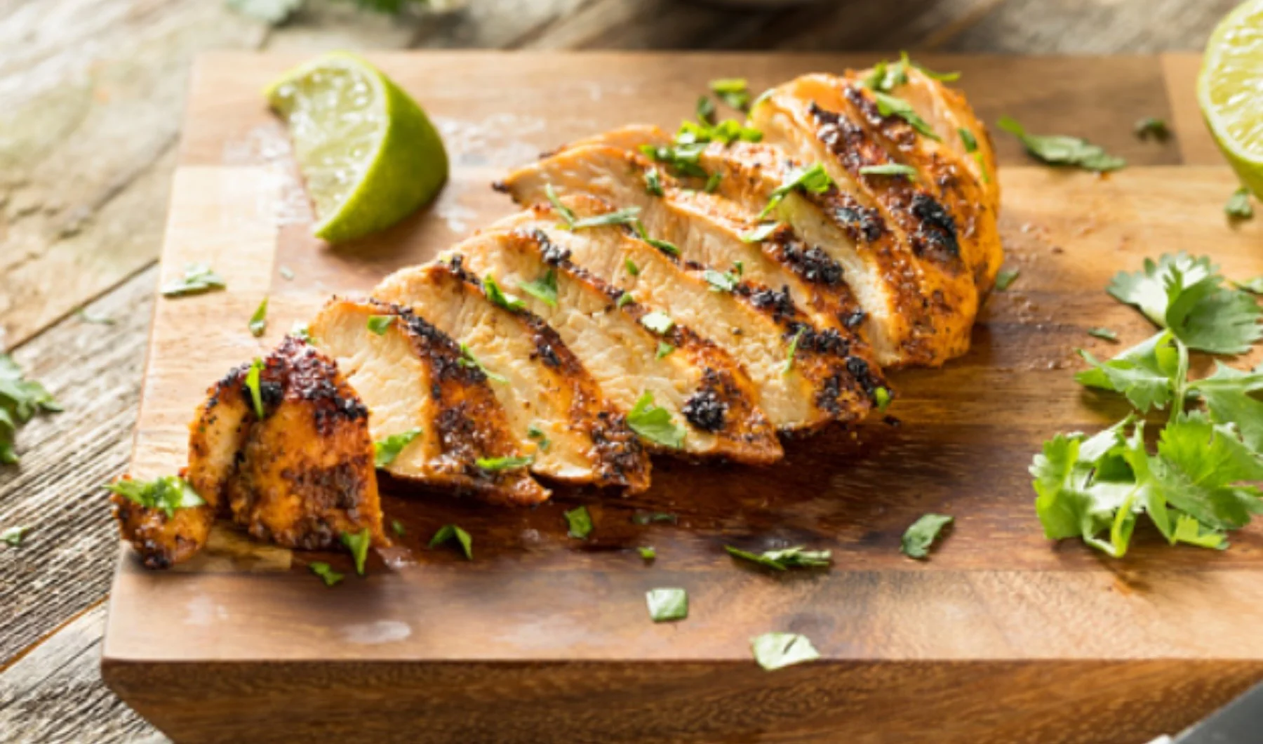 Pechuga de pollo a la parrilla en rebanadas, con cilantro picado y rodajas de limón, sobre una tabla de madera