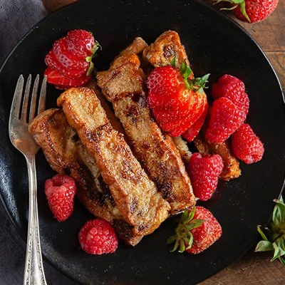 Tostadas francesas con fresas y frambuesas en un plato negro, con un tenedor de metal a la izquierda