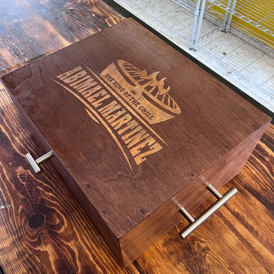 Caja de madera oscura con agarraderas metálicas y un grabado con el texto