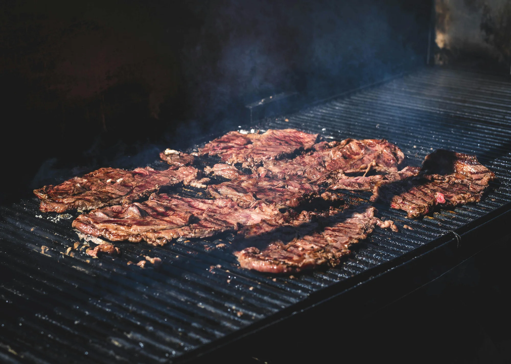 Arrachera asándose sobre una parrilla de metal con humo saliendo de la carne, mostrando el proceso de cocción