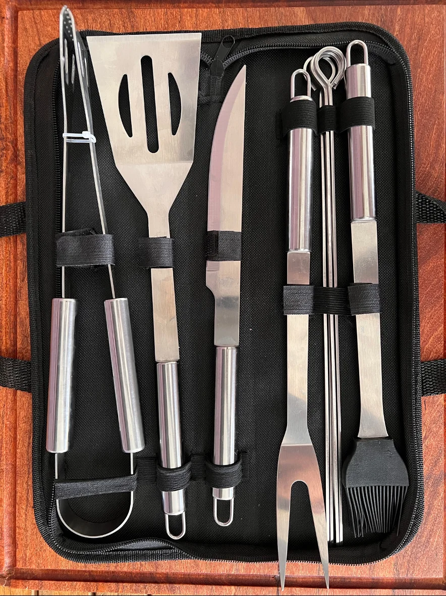 Juego de utensilios de parrilla de acero inoxidable en un estuche negro, con espátula, cuchillo, pinzas, brochetas, tenedor y brocha