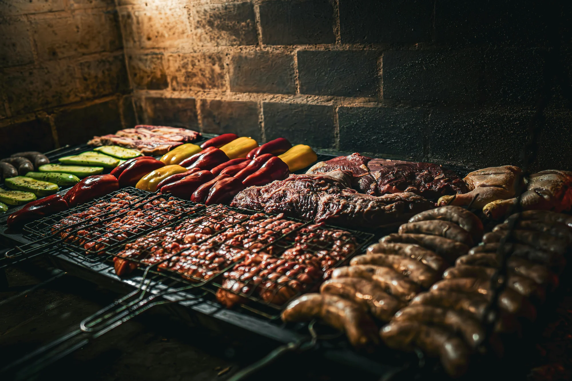Parrilla con carne asada, chorizos, morcillas, pimientos rojos y amarillos, y calabacitas, sobre un fondo de ladrillo