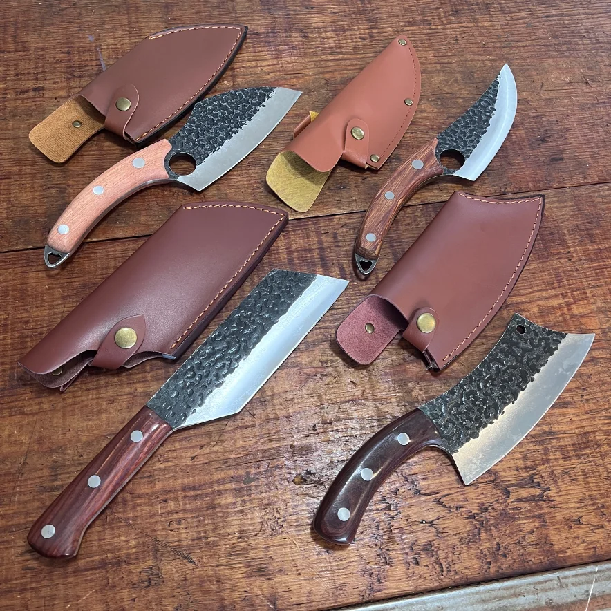 Cuatro cuchillos de hoja forjada con mangos de madera y sus fundas de piel marrón sobre una mesa de madera rústica