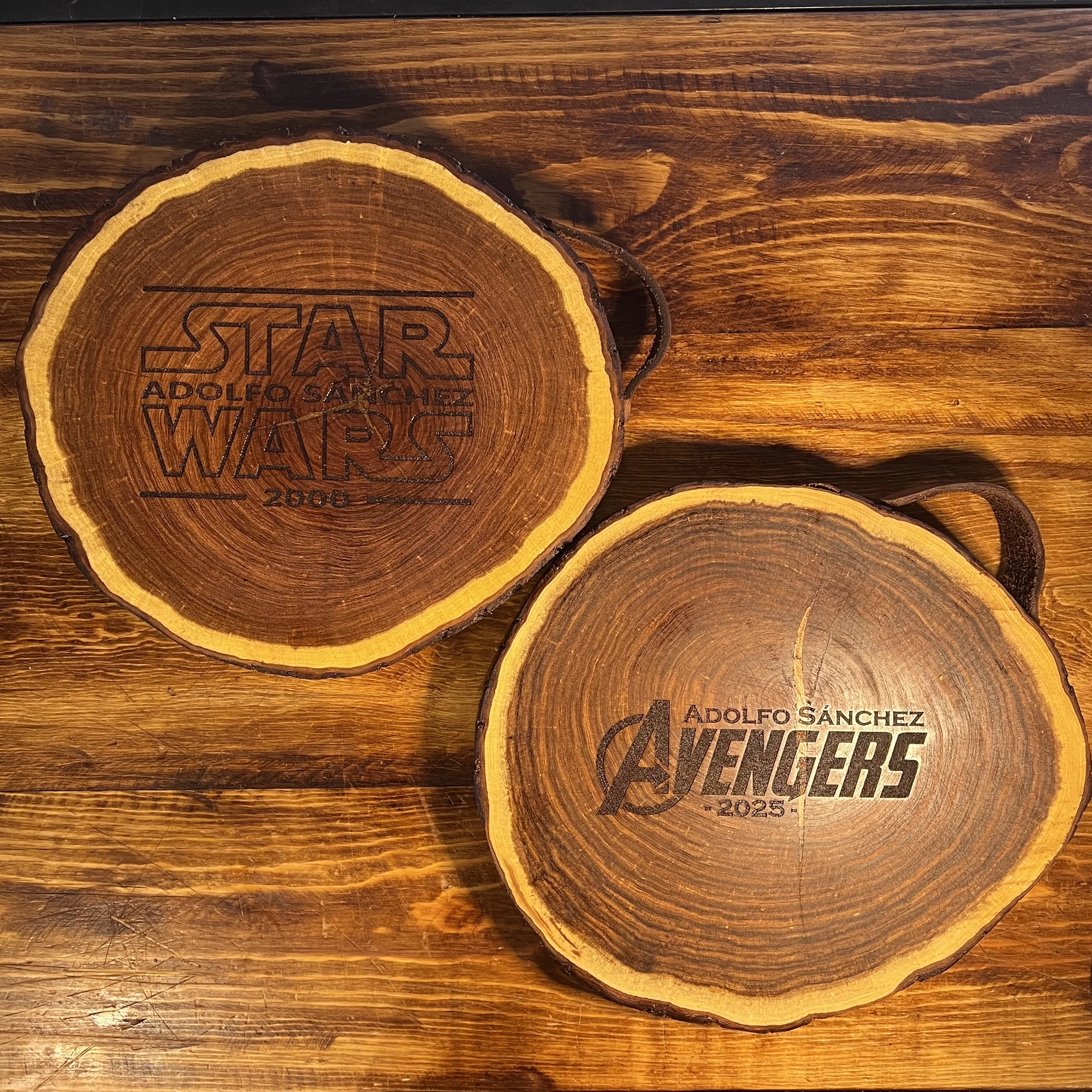 Dos tablas de madera rústicas con corteza, grabadas con los logos de Star Wars y Avengers, y el nombre
