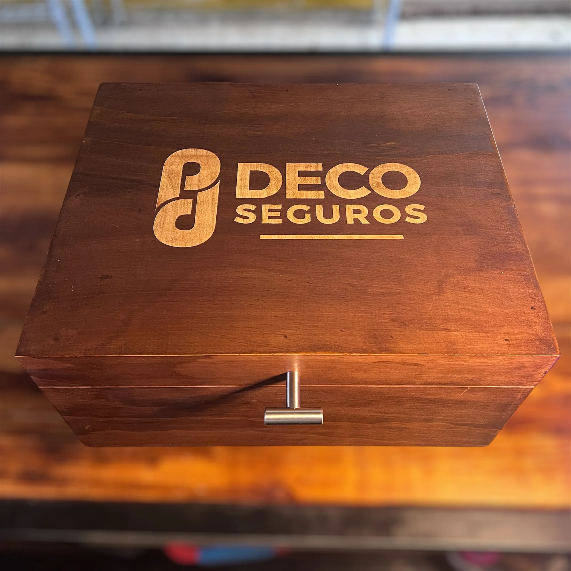 Caja de madera oscura con un grabado claro que dice "DECO SEGUROS" y un tirador metálico en el frente