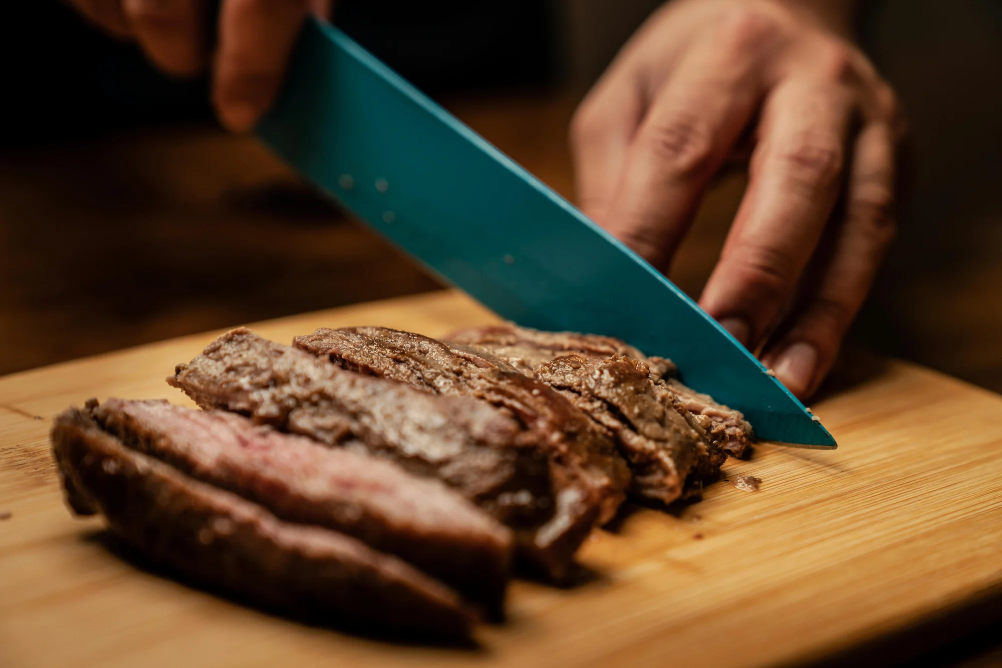 Mano cortando arrachera cocida en una tabla de madera clara, mostrando el interior rosado de la carne